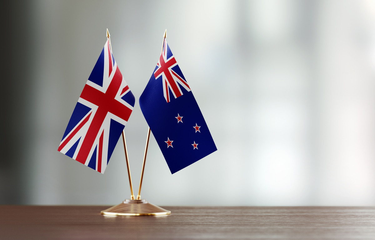 Two miniature flags of the United Kingdom and New Zealand displayed side by side on a wooden surface.