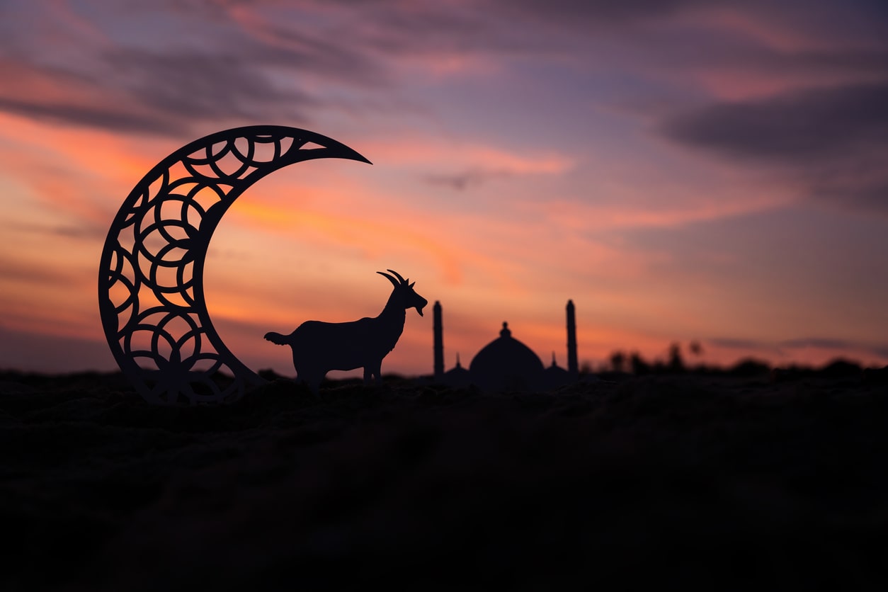 Eid al-Adha with a goat, crescent moon, and mosque at sunset, reflecting sacrifice and faith