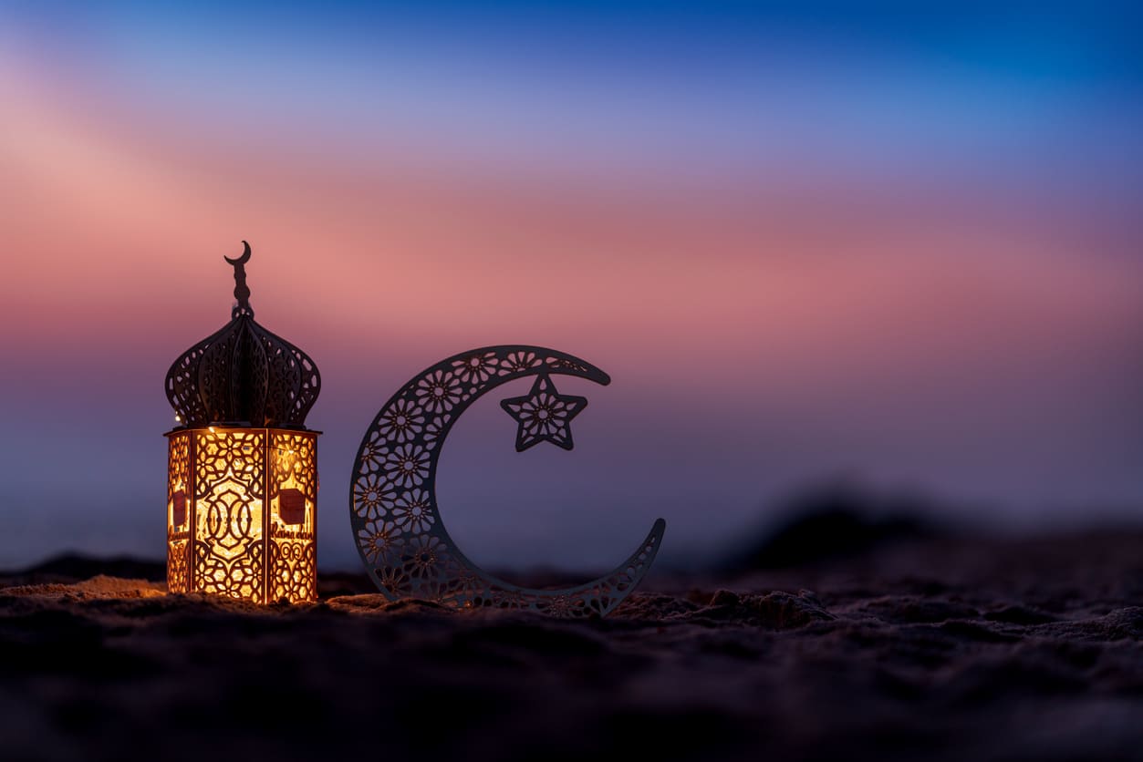 A glowing lantern beside a decorative crescent moon and star, set against a serene twilight sky, capturing the peaceful and reflective spirit of Ramadan