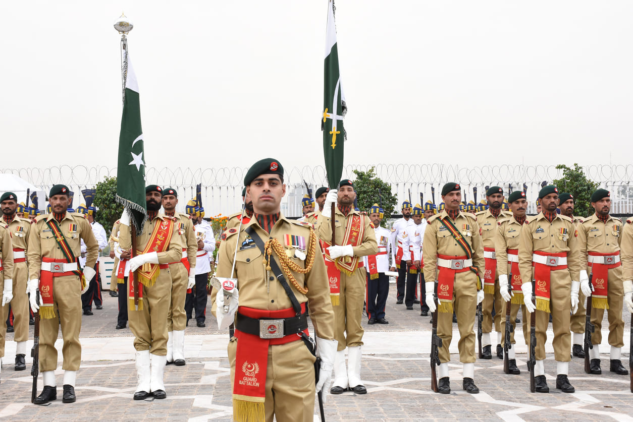 A ceremonial parade of Pakistani soldiers in uniform, proudly holding the national flag to honor Defence Day.