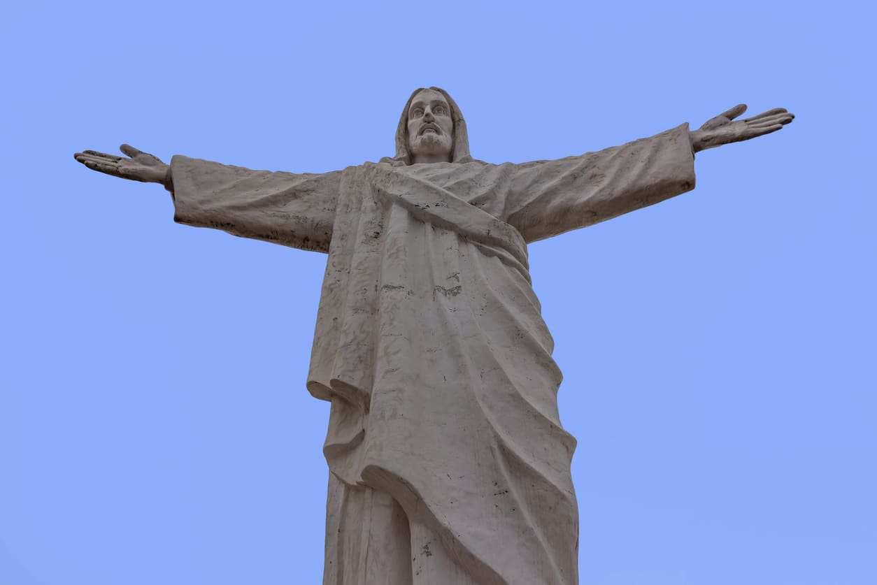 A towering statue of Christ with outstretched arms against a clear sky, symbolizing peace and divine love.