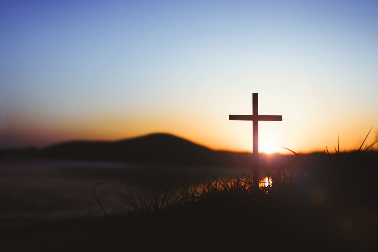 A cross stands atop a hill, illuminated by the warm hues of a serene sunrise, symbolizing peace and faith.