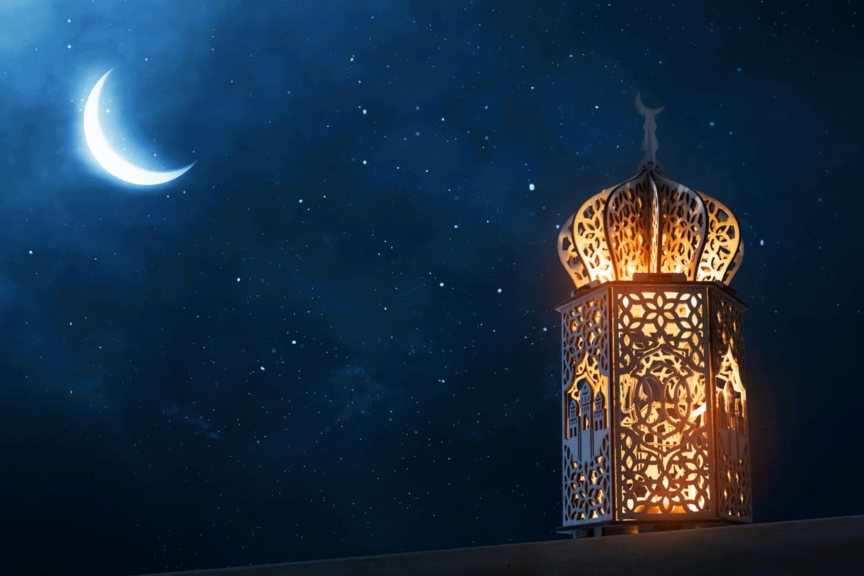 A glowing crescent moon beside an intricately designed lantern, symbolizing the spiritual beginning of Ramadan.