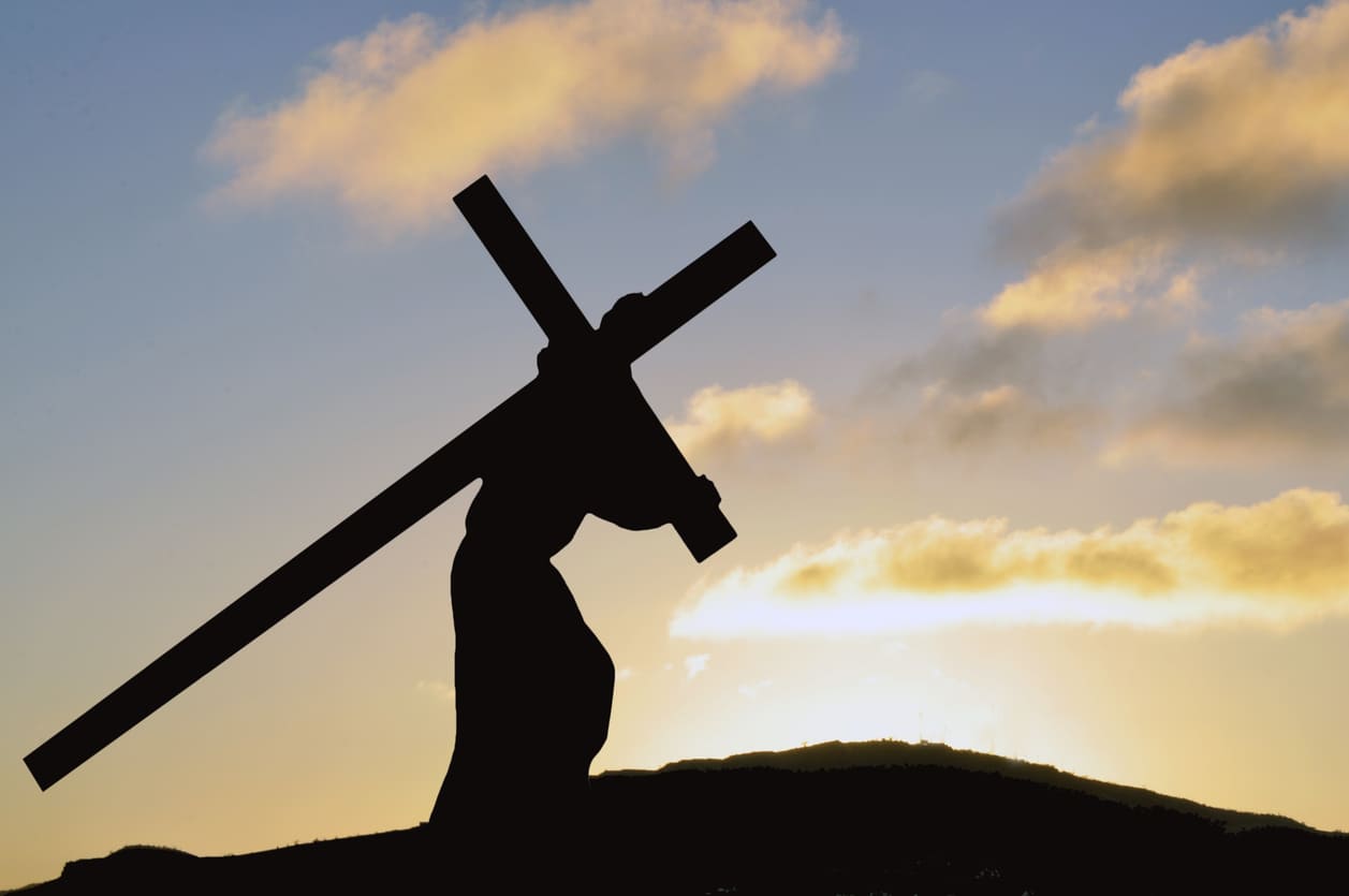 A silhouette of a person carrying a large cross against a backdrop of a sunset sky, symbolizing the suffering of Christ on Good Friday.