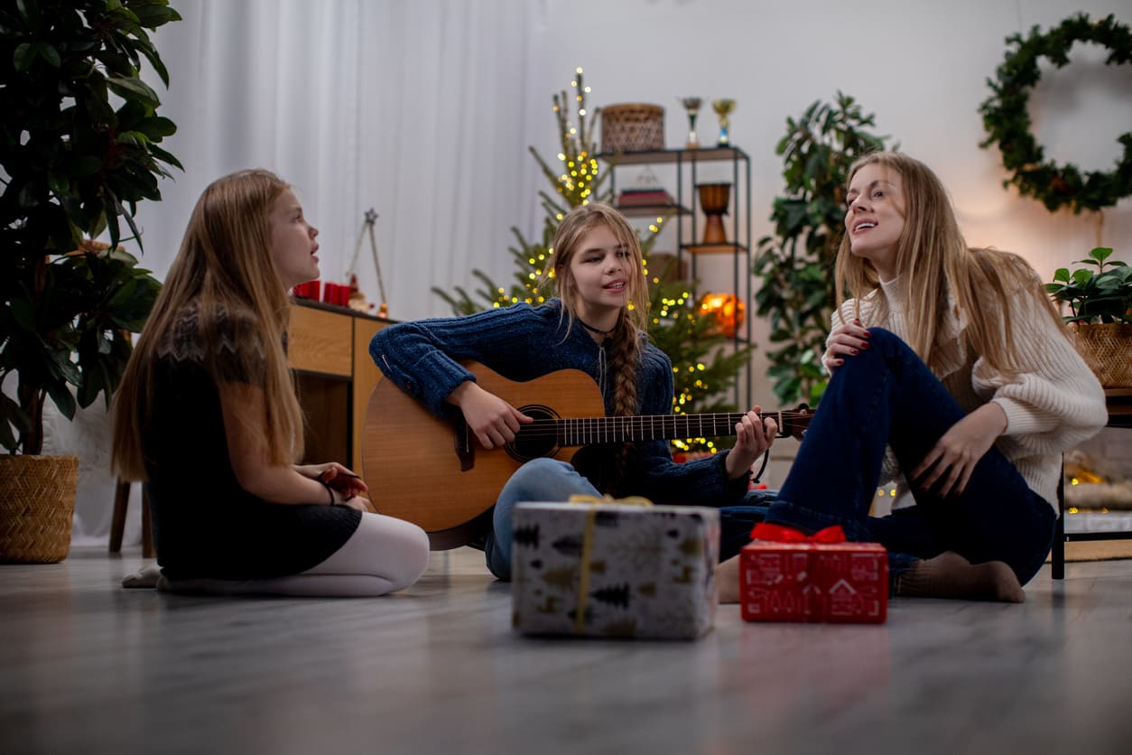 Three girls sing and play guitar in a cozy, festive setting on the Second Day of Christmas.