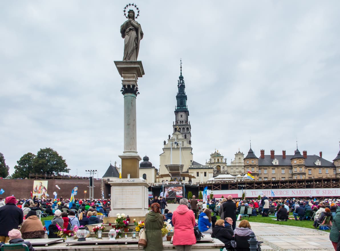 A large gathering of pilgrims at Jasna Góra Monastery in Poland, attending an outdoor religious service in a solemn and spiritual atmosphere.