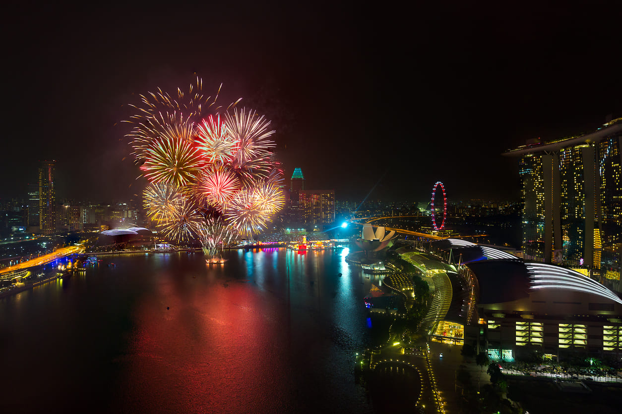A stunning fireworks display over Marina Bay, with vibrant lights reflecting on the water and Singapore's city skyline illuminated at night.