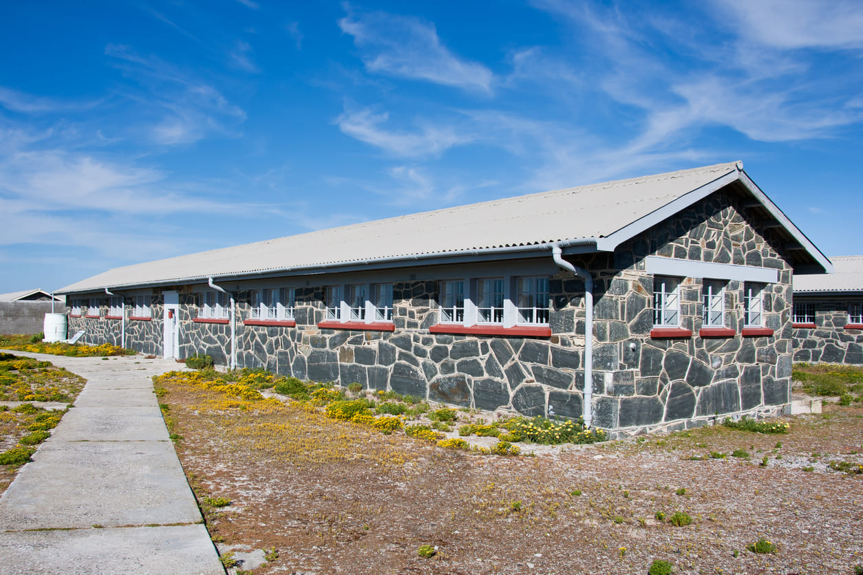 A stone-walled prison building on Robben Island under a clear blue sky, symbolizing the resilience and history of South Africa's freedom struggle.