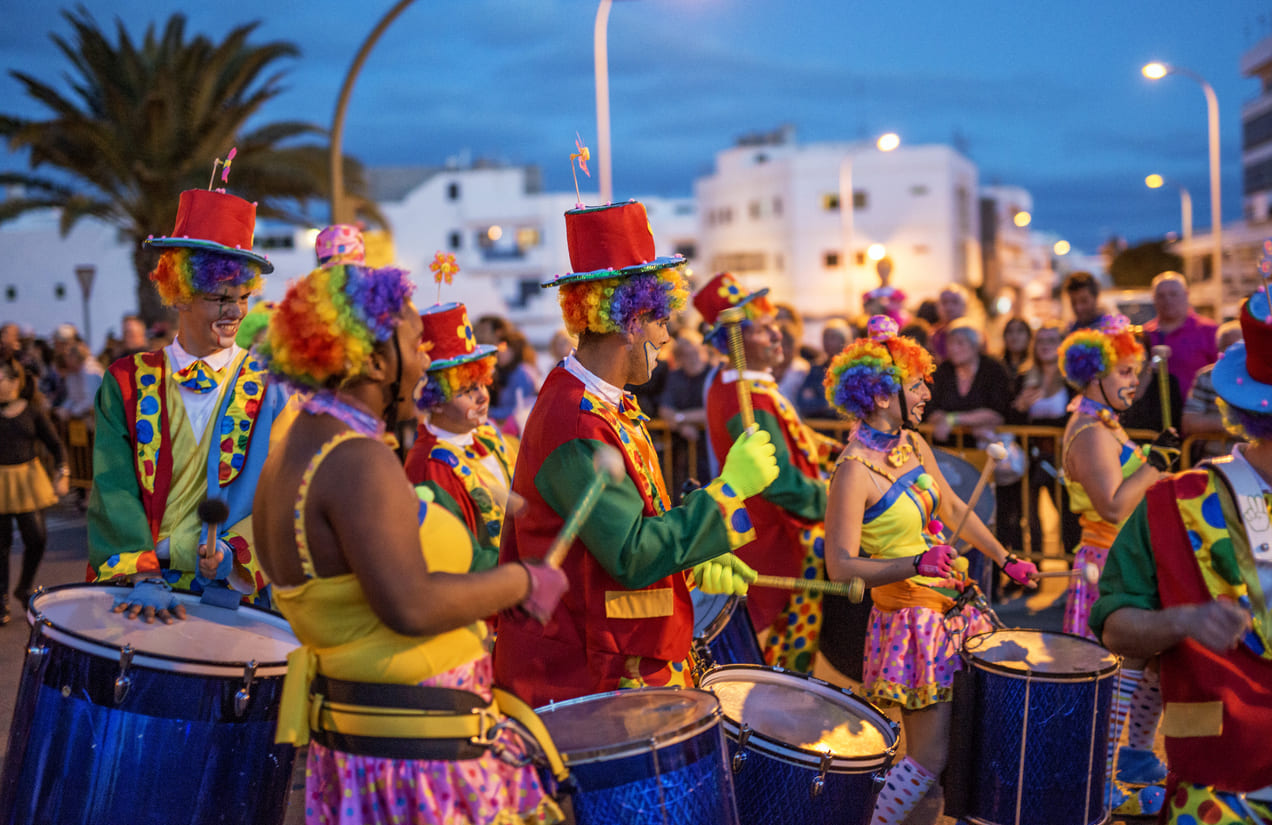 A lively scene from the Grand Parade of Carnival Monday, where participants in colorful clown costumes play drums and celebrate amid cheering crowds.