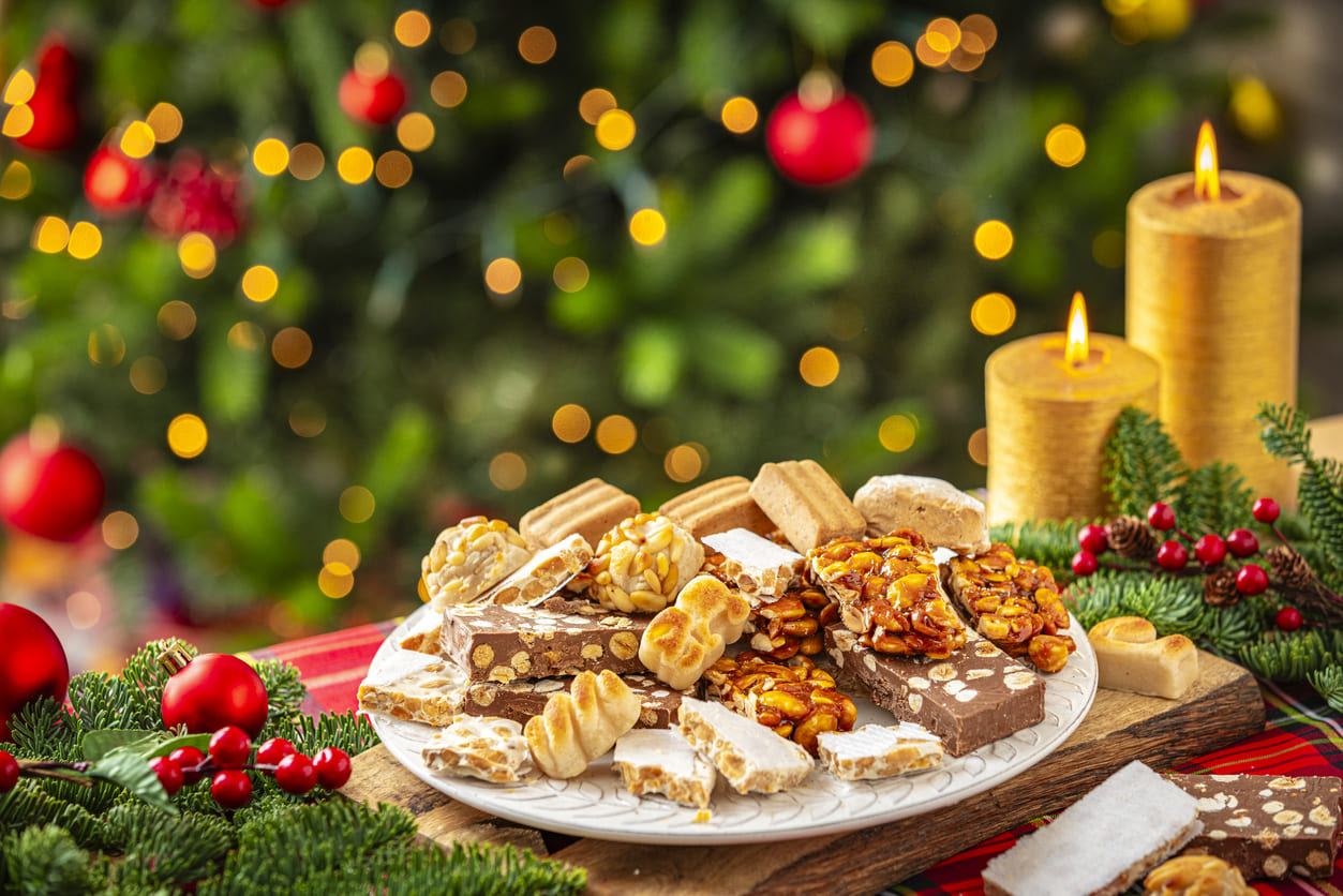 A beautifully arranged plate of traditional Spanish Christmas sweets, including turrón, polvorones, and mazapán, set against a cozy holiday backdrop with candles and festive decorations.