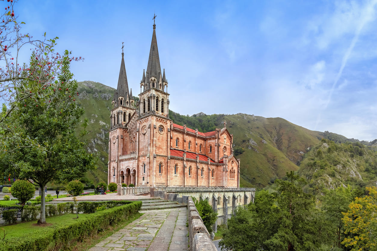 The Basilica de Santa María la Real de Covadonga stands elegantly amidst the lush green mountains of Asturias, showcasing its Neo-Romanesque architecture and deep historical significance.