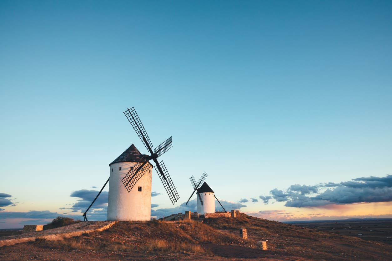 A breathtaking view of the iconic windmills of Castile-La Mancha, standing atop rolling hills at sunset, symbolizing the region's heritage and its connection to Don Quixote.