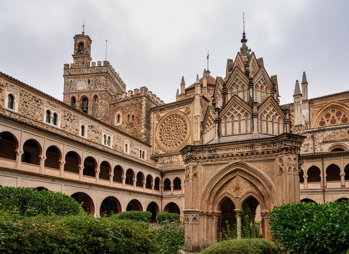 A stunning medieval monastery with intricate Gothic and Mudejar architectural details, surrounded by lush greenery, symbolizing Extremadura's rich cultural and religious heritage.