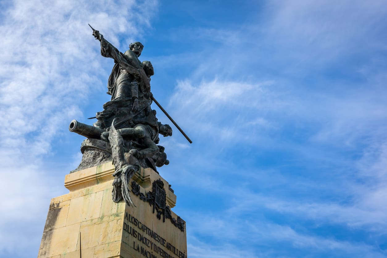 A striking monument featuring a heroic figure atop a pedestal, surrounded by cannons and soldiers, symbolizing bravery and resistance.