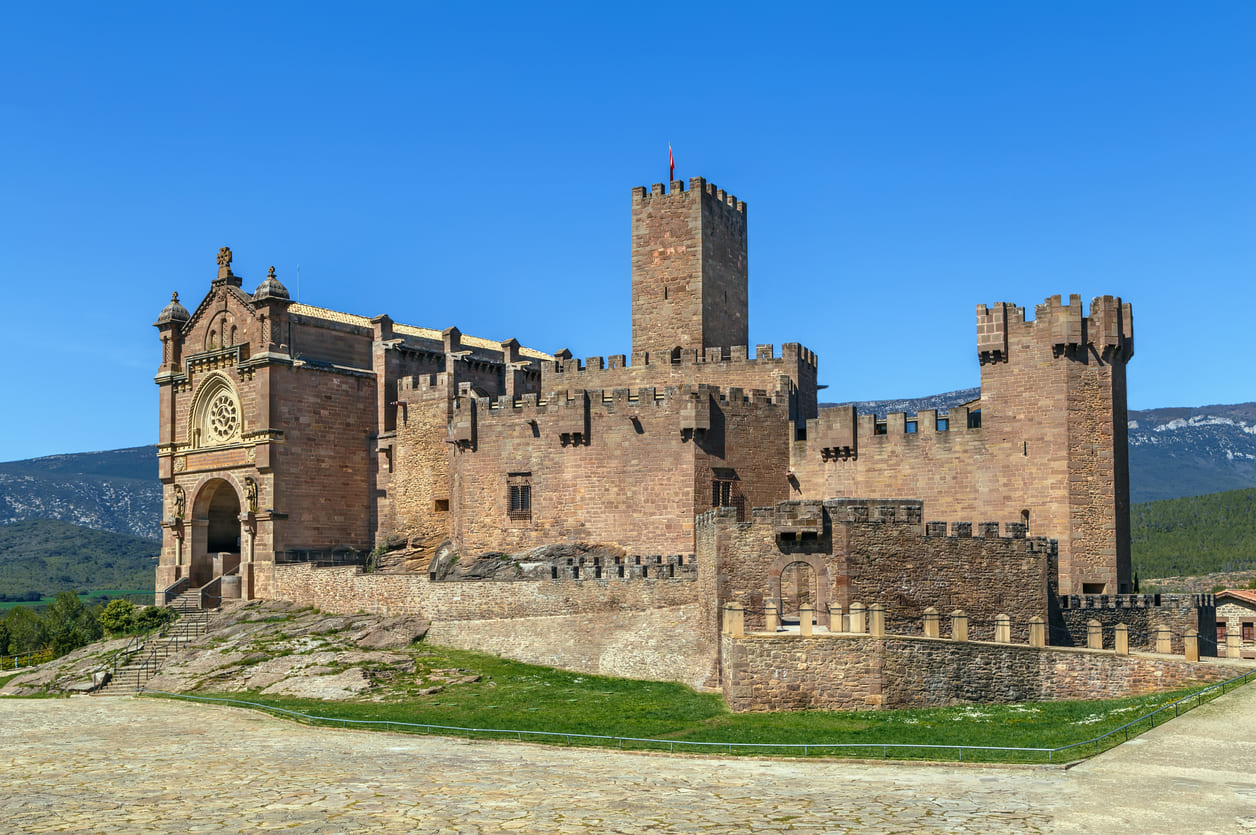 A historic stone castle with fortified towers and an ornate entrance, set against a scenic mountainous backdrop, symbolizing Navarre's rich heritage.