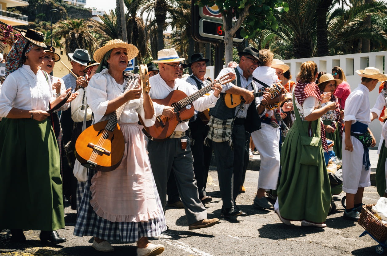 A joyful group dressed in traditional Canarian clothing plays folk music and sings while celebrating the Day of the Canary Islands in an outdoor festive setting.