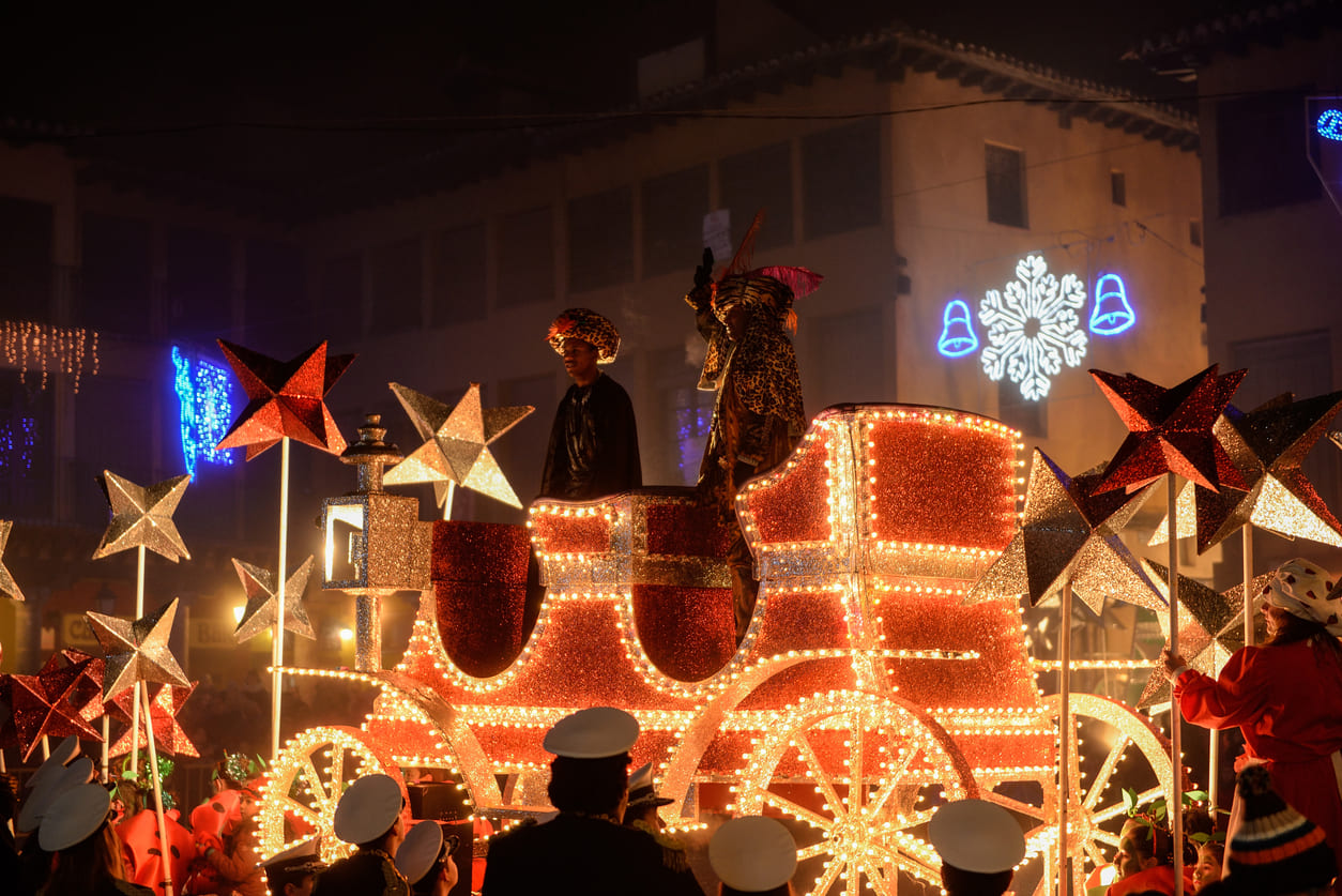 A vibrant Cabalgata de Reyes parade features a beautifully illuminated float carrying one of the Three Kings, surrounded by festive decorations and joyful spectators.