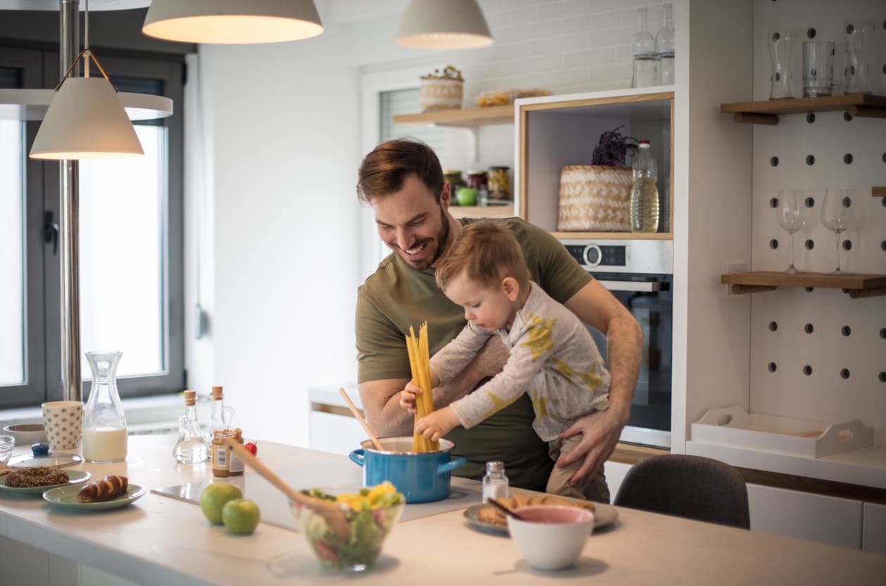 A smiling father and his young child share a special moment cooking together in a cozy kitchen.