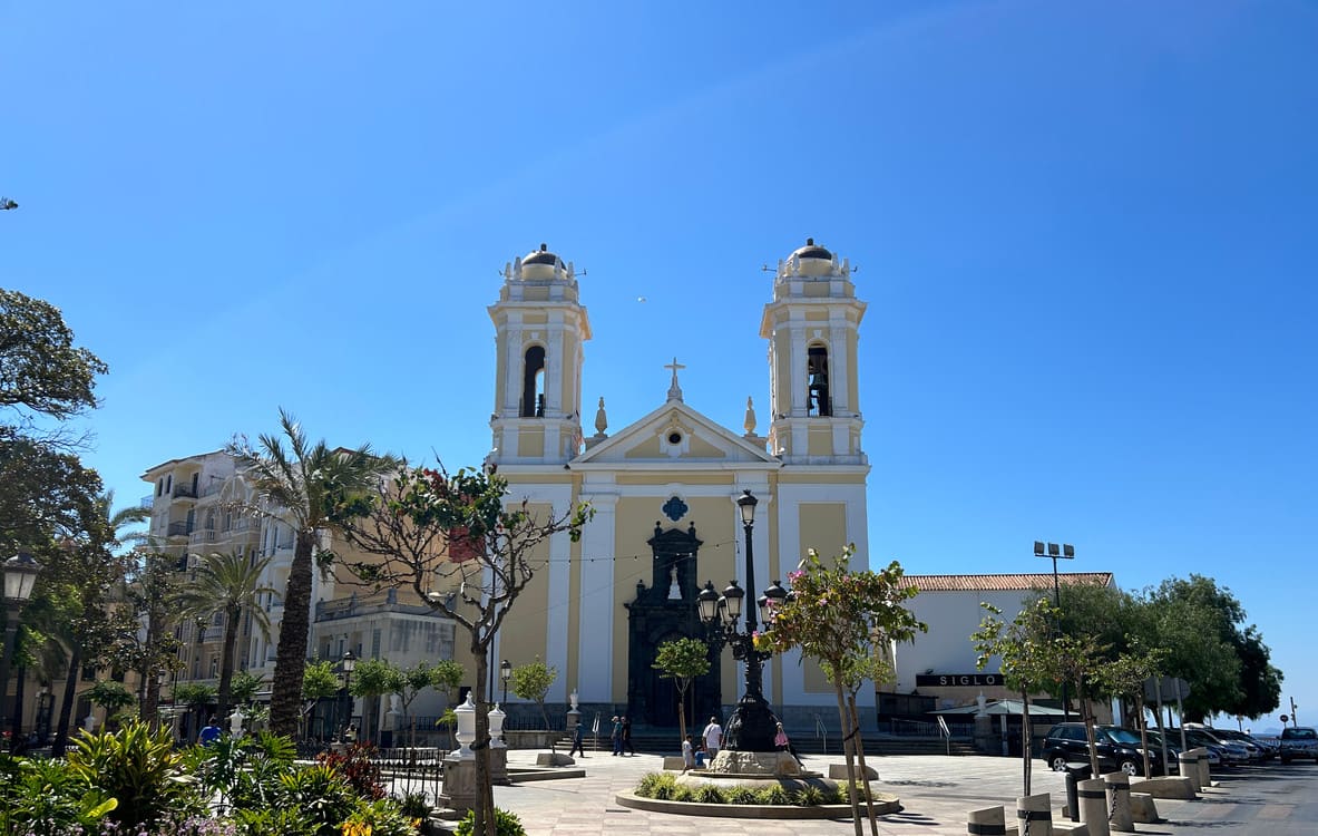 A beautiful view of the Church of Santa María de África in Ceuta, Spain, with its twin bell towers and serene plaza under a clear blue sky.