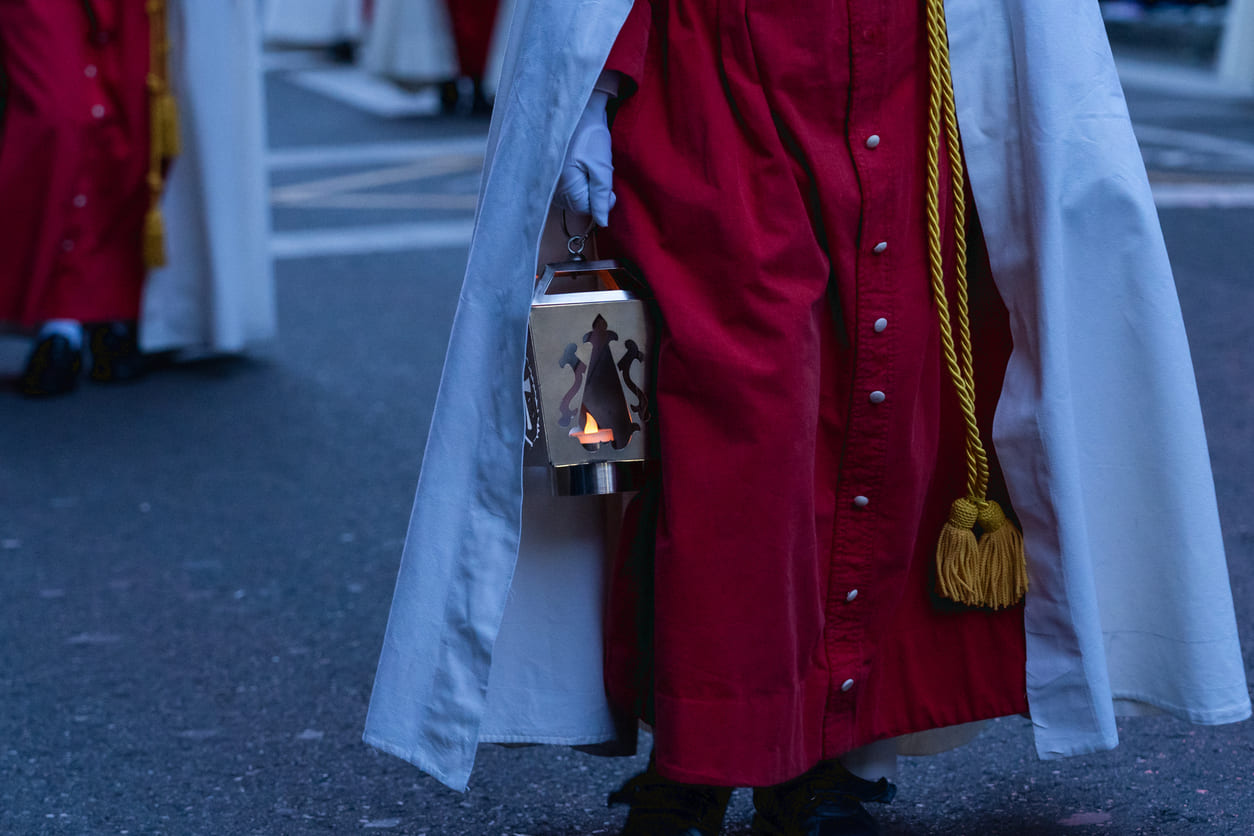 A participant in a Semana Santa procession walks solemnly, dressed in traditional robes and carrying a lantern, symbolizing Christ's Passion on Good Friday.