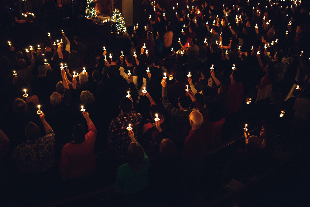 A congregation gathers in a darkened church, holding candles in a solemn Easter Vigil ceremony, marking the transition from mourning to resurrection on Holy Saturday.