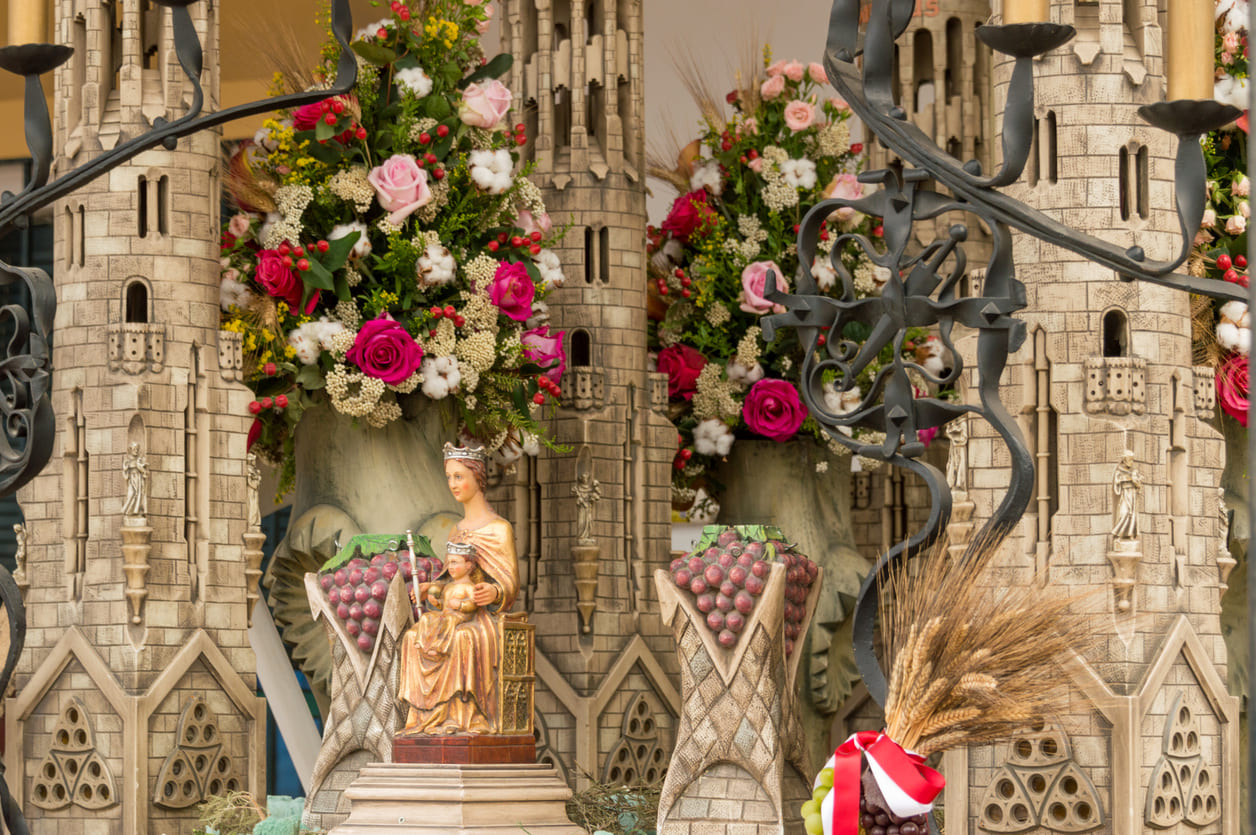 A richly decorated religious altar featuring a statue of the Virgin Mary with floral arrangements, symbolic ornaments, and architectural elements, reflecting devotion and tradition.