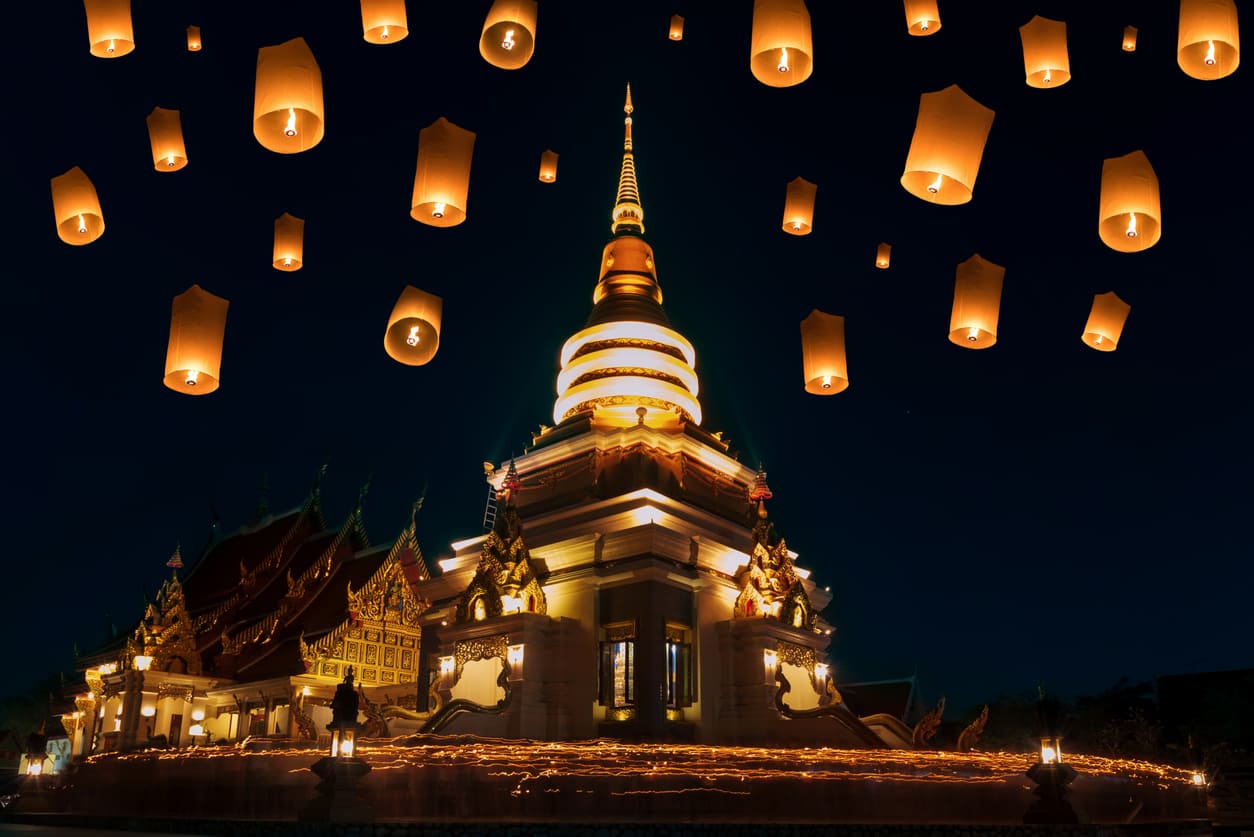 Glowing lanterns float into the night sky above a beautifully illuminated temple, creating a serene and spiritual scene.