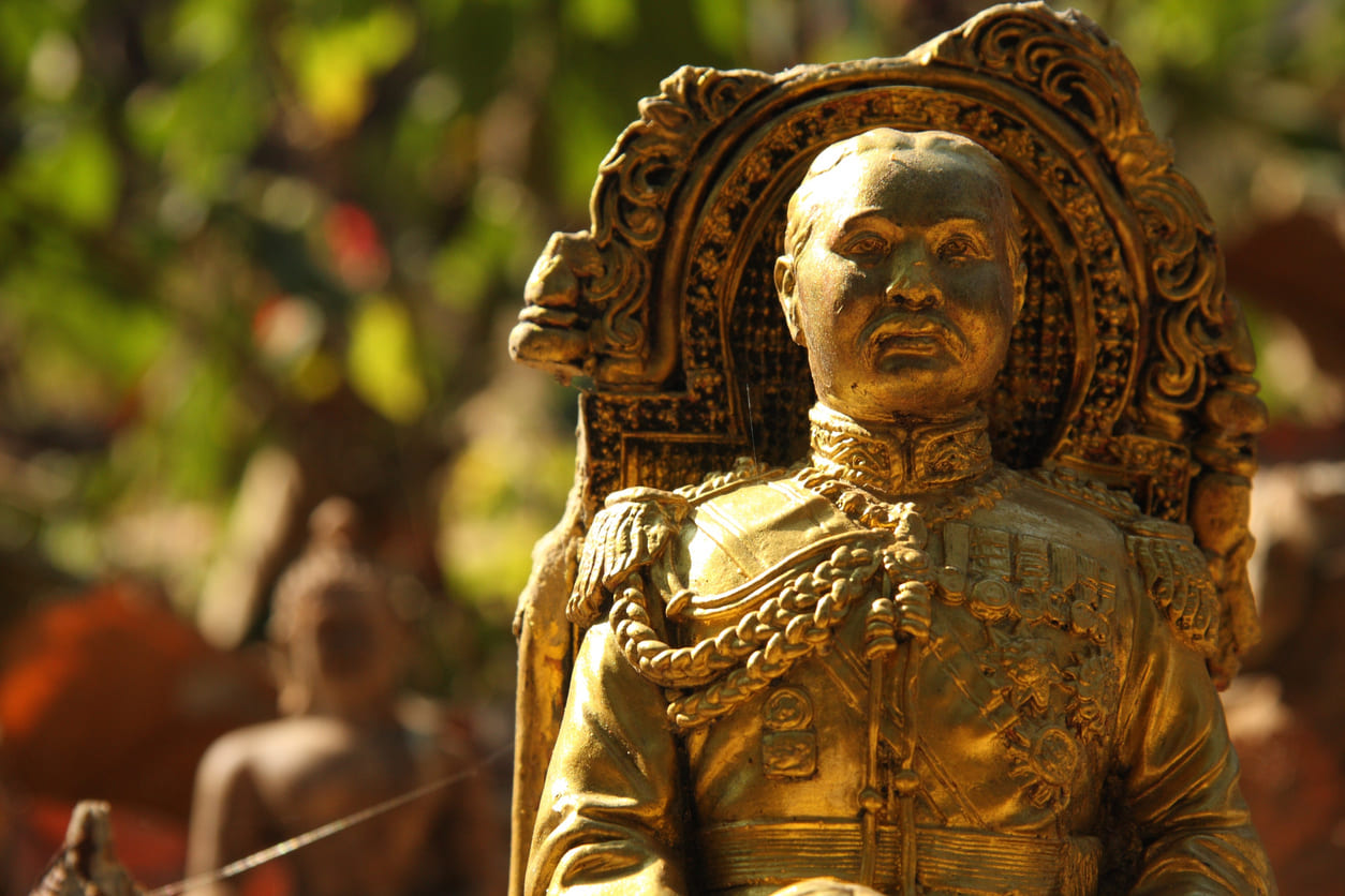 A golden statue of King Rama V sits elegantly in a Buddhist temple, surrounded by soft natural light and intricate details.