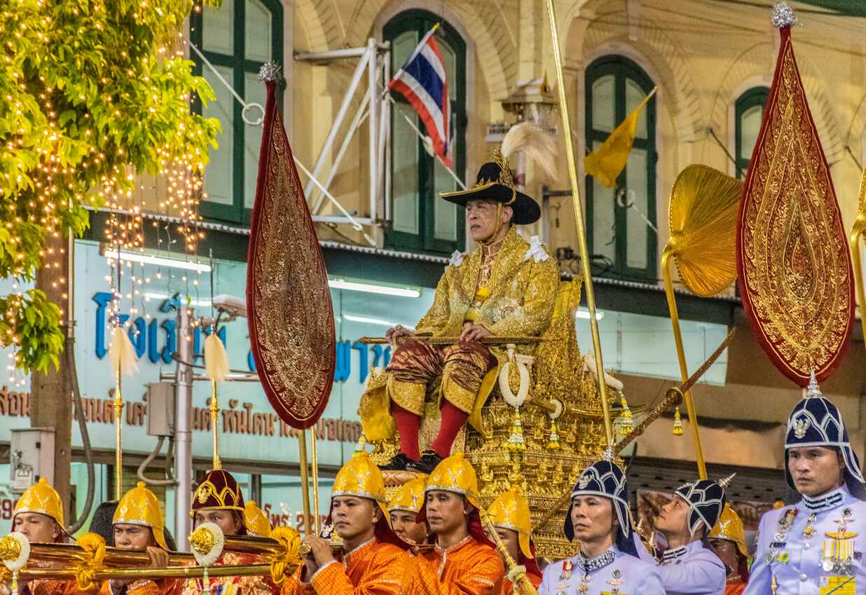 King Maha Vajiralongkorn sits on a golden palanquin carried by royal guards, surrounded by ornate ceremonial decorations during the coronation procession in Bangkok.