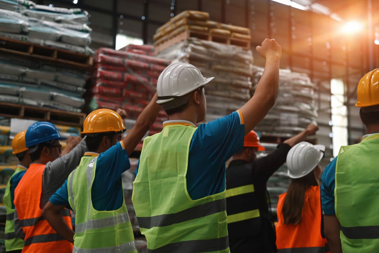Workers stand close together, raising their fists in solidarity during a Labor Day gathering.