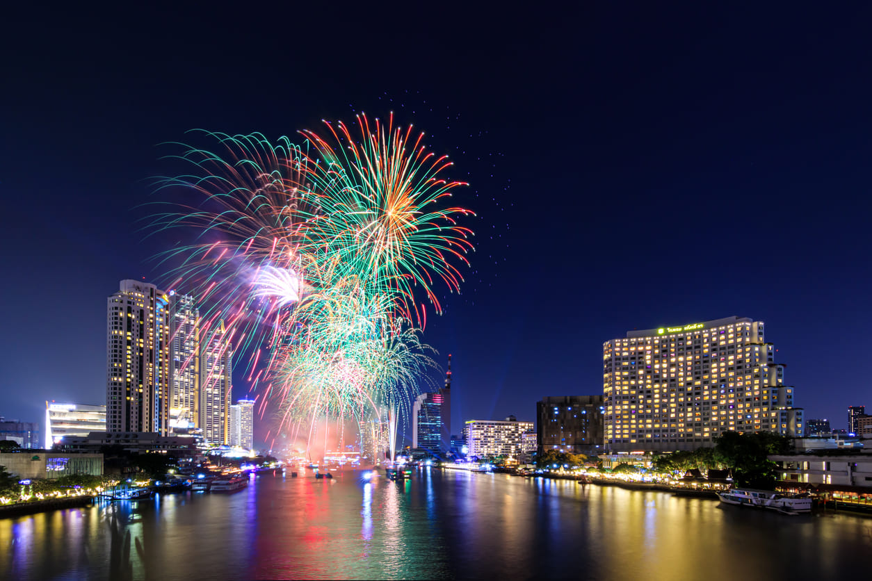 A vibrant display of fireworks bursts over Bangkok's illuminated skyline, reflecting the festive spirit of New Year's Day celebrations in Thailand.