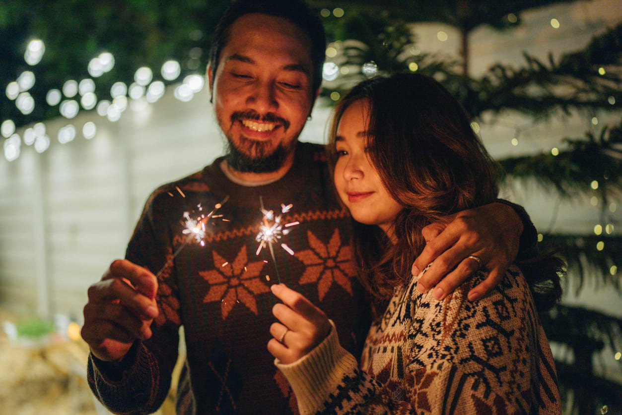 A cheerful couple holding sparklers under twinkling lights, capturing the festive warmth of New Year's Eve celebrations in Thailand.