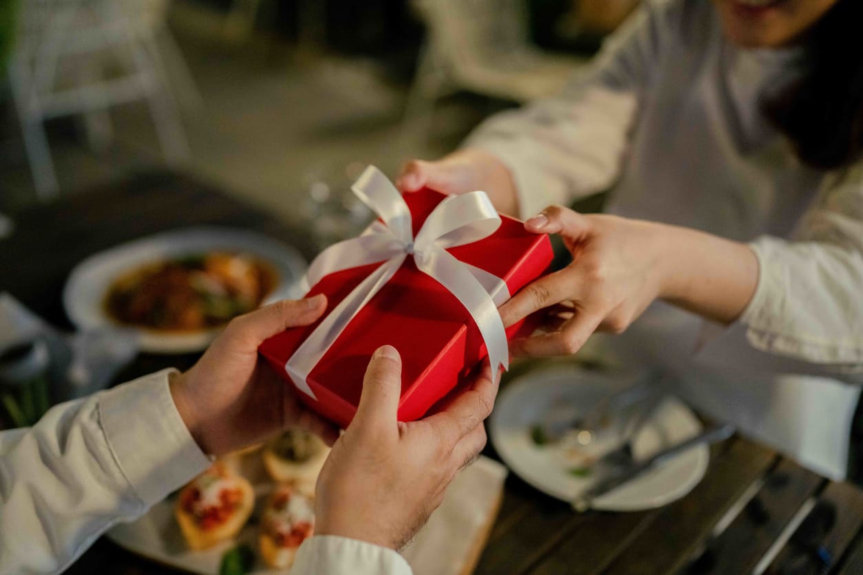 A close-up of a couple exchanging a red gift box, symbolizing the romantic gestures shared on Valentine's Day in Thailand.