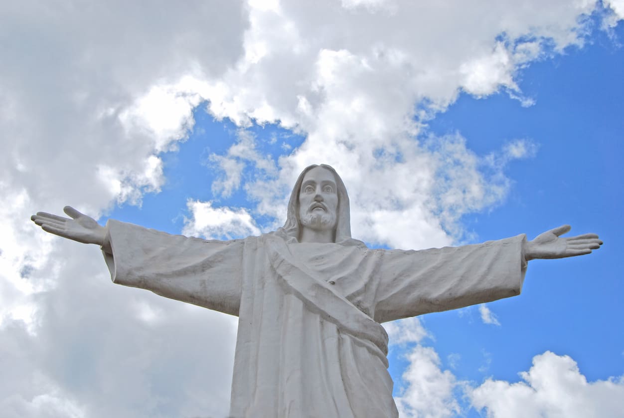 Statue of Jesus Christ with open arms against a bright, cloudy sky, symbolizing peace, hope, and the spirit of Ascension Day.