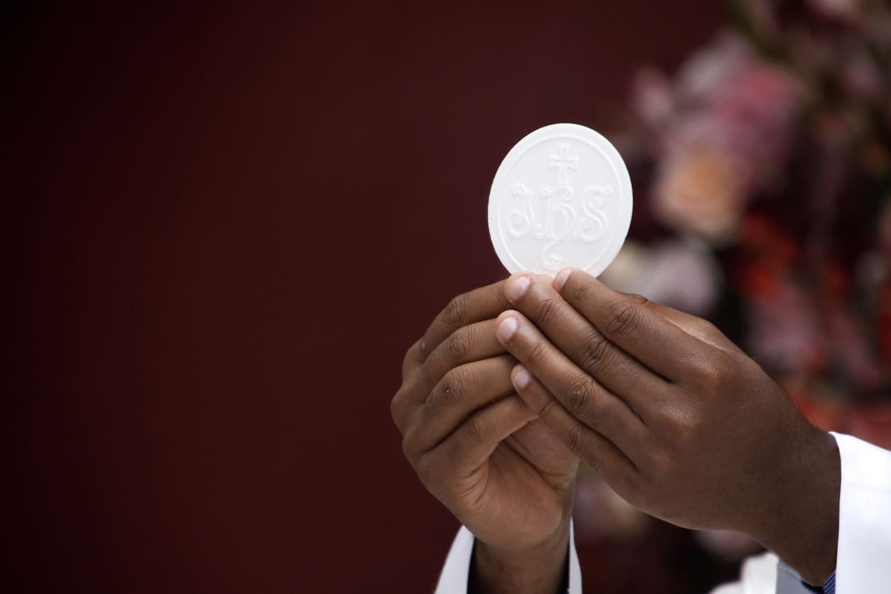 Holding the holy wafer during Communion, symbolizing the Body of Christ in a sacred church ritual.