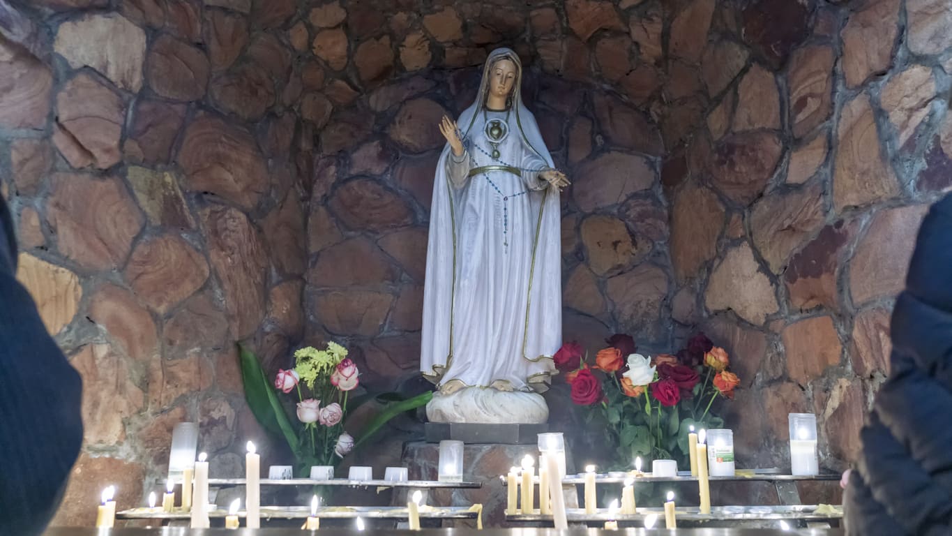 A statue of the Virgin Mary surrounded by candles and flowers, reflecting devotion and prayer during the Feast of the Immaculate Conception.