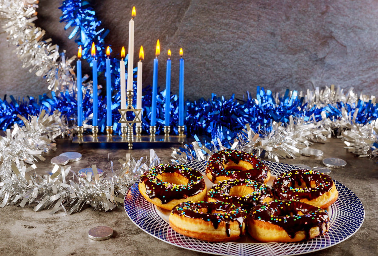 A lit menorah with festive doughnuts, celebrating Hanukkah traditions.