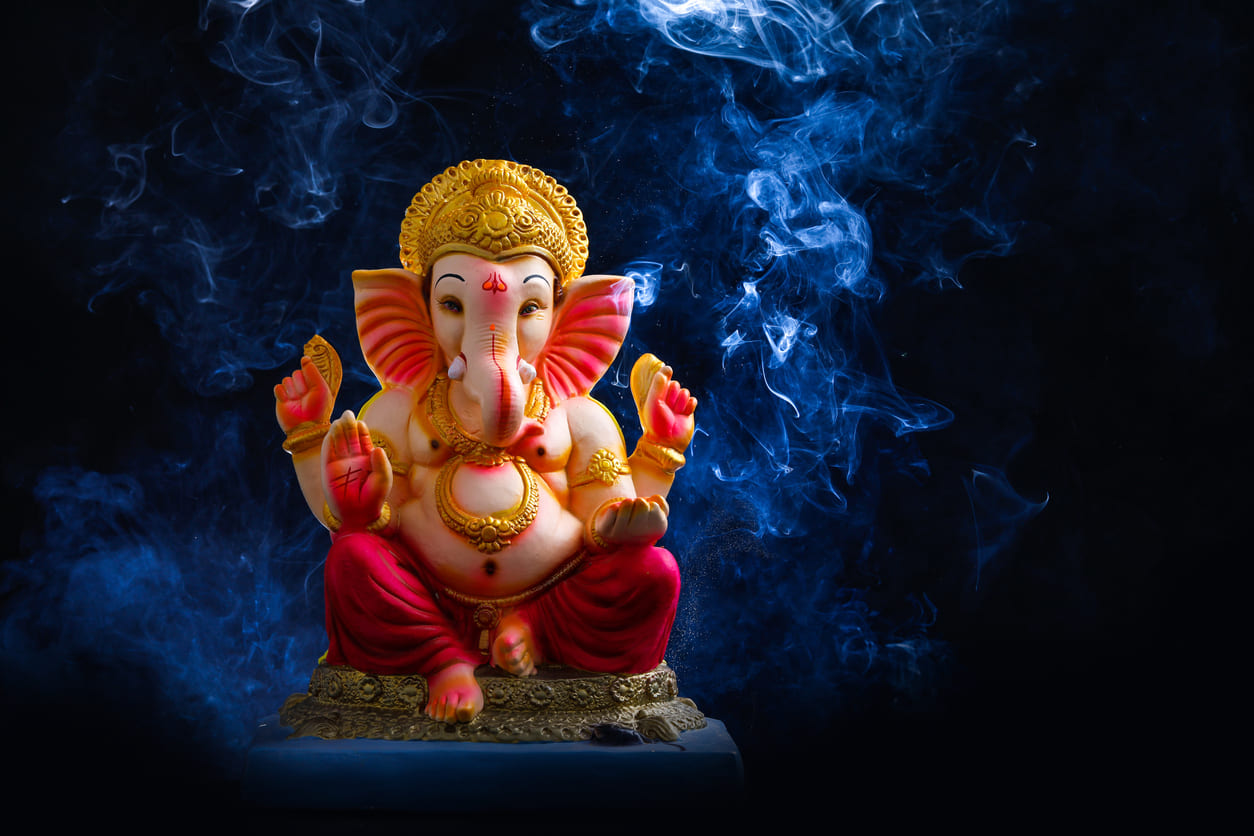 A colorful Lord Ganesha idol sits gracefully amidst swirling incense smoke, evoking a sense of devotion and spirituality.