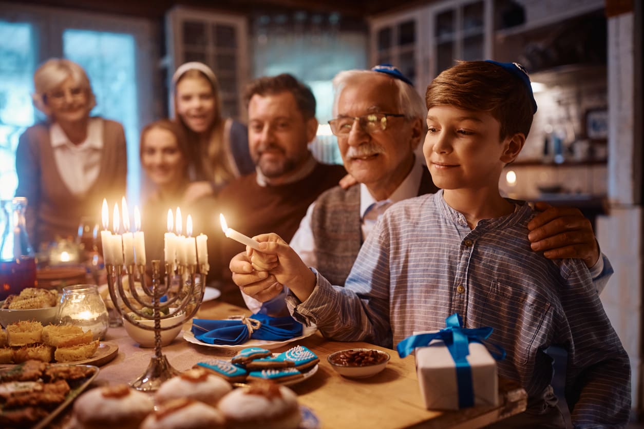 A family celebrates the last night of Hanukkah, lighting the menorah together amidst festive food and gifts.