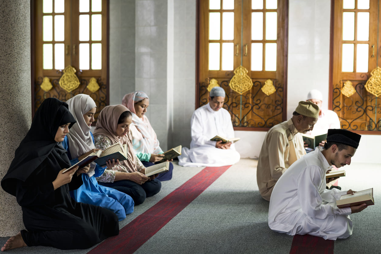 A group of people sits in a mosque, reading the Qur'an and praying together during Laylat al-Qadr.