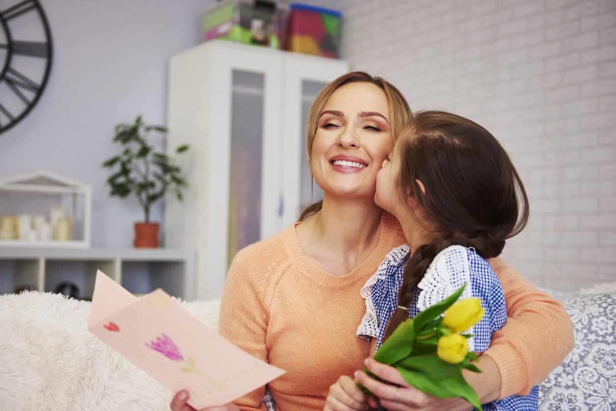 A child holds flowers and a handmade card, capturing the warmth and love of Mother's Day.