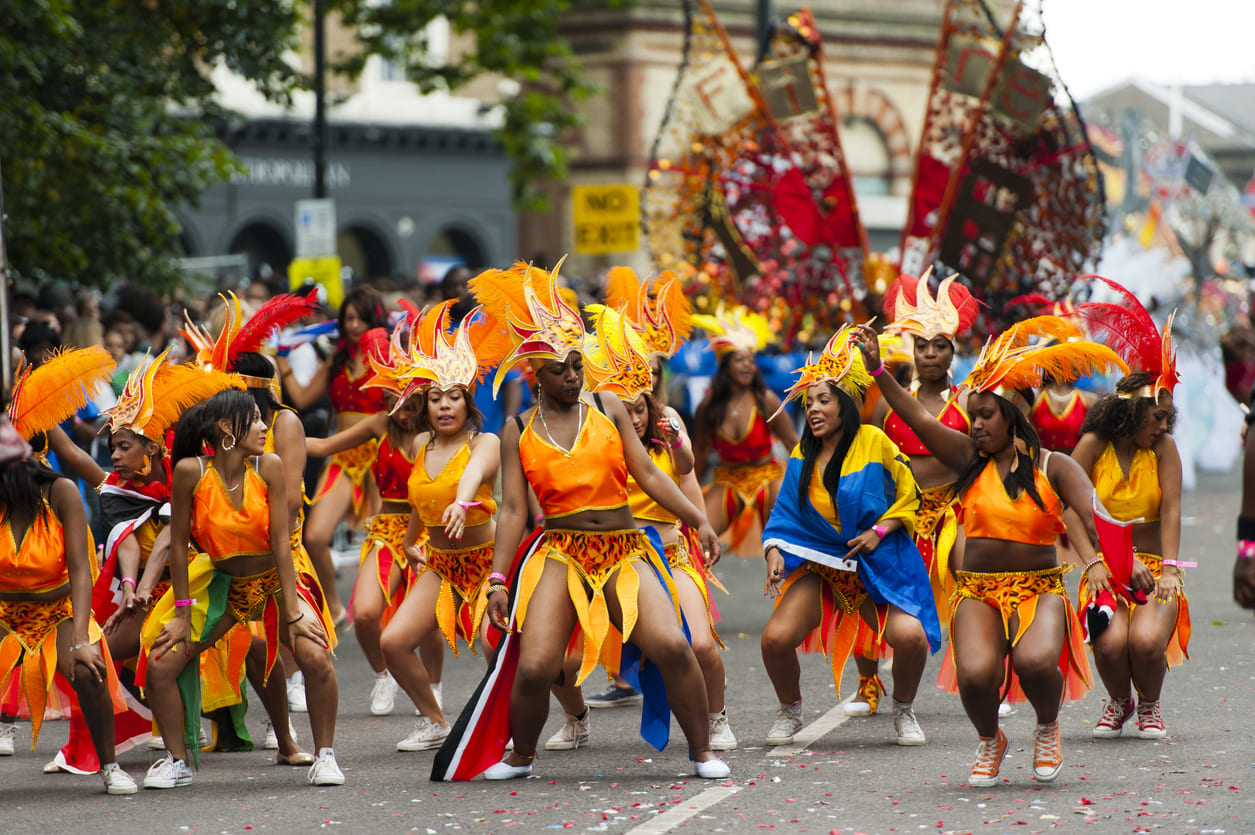 A vibrant street parade with dancers in colorful costumes, celebrating Caribbean culture and the contributions of the Windrush generation.