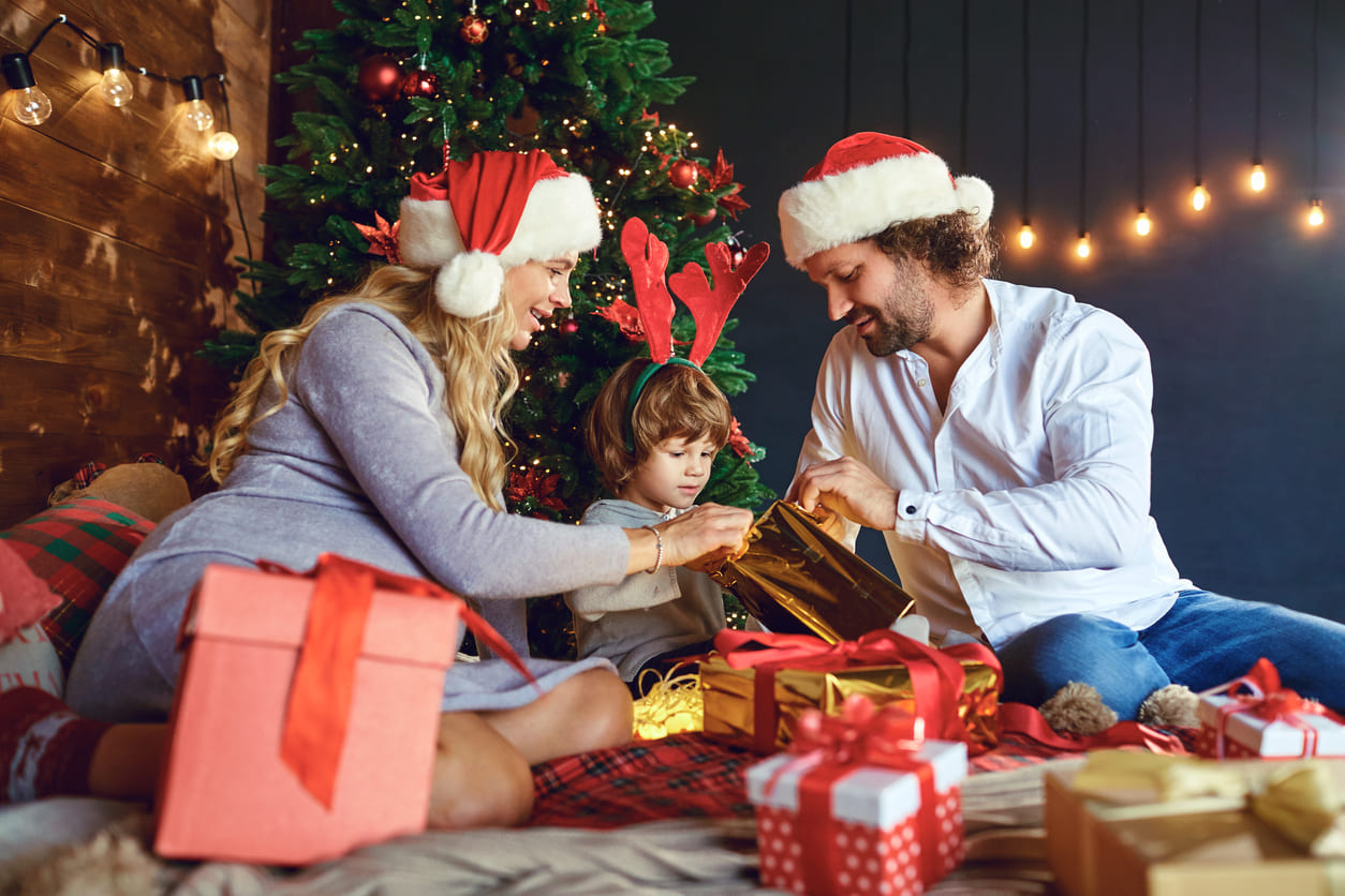 A family joyfully opens gifts by the Christmas tree, sharing in the festive spirit.