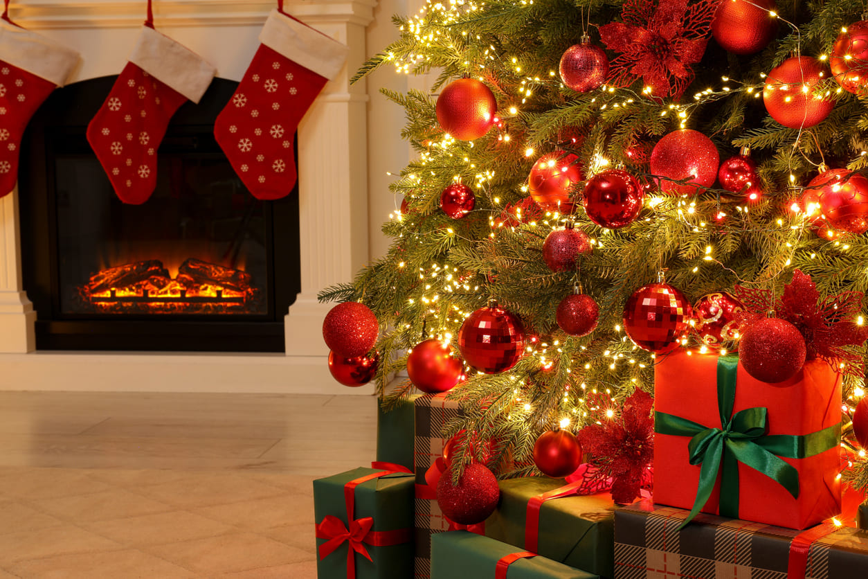 A beautifully decorated Christmas tree glows with lights, surrounded by gifts, while stockings hang by the cozy fireplace.