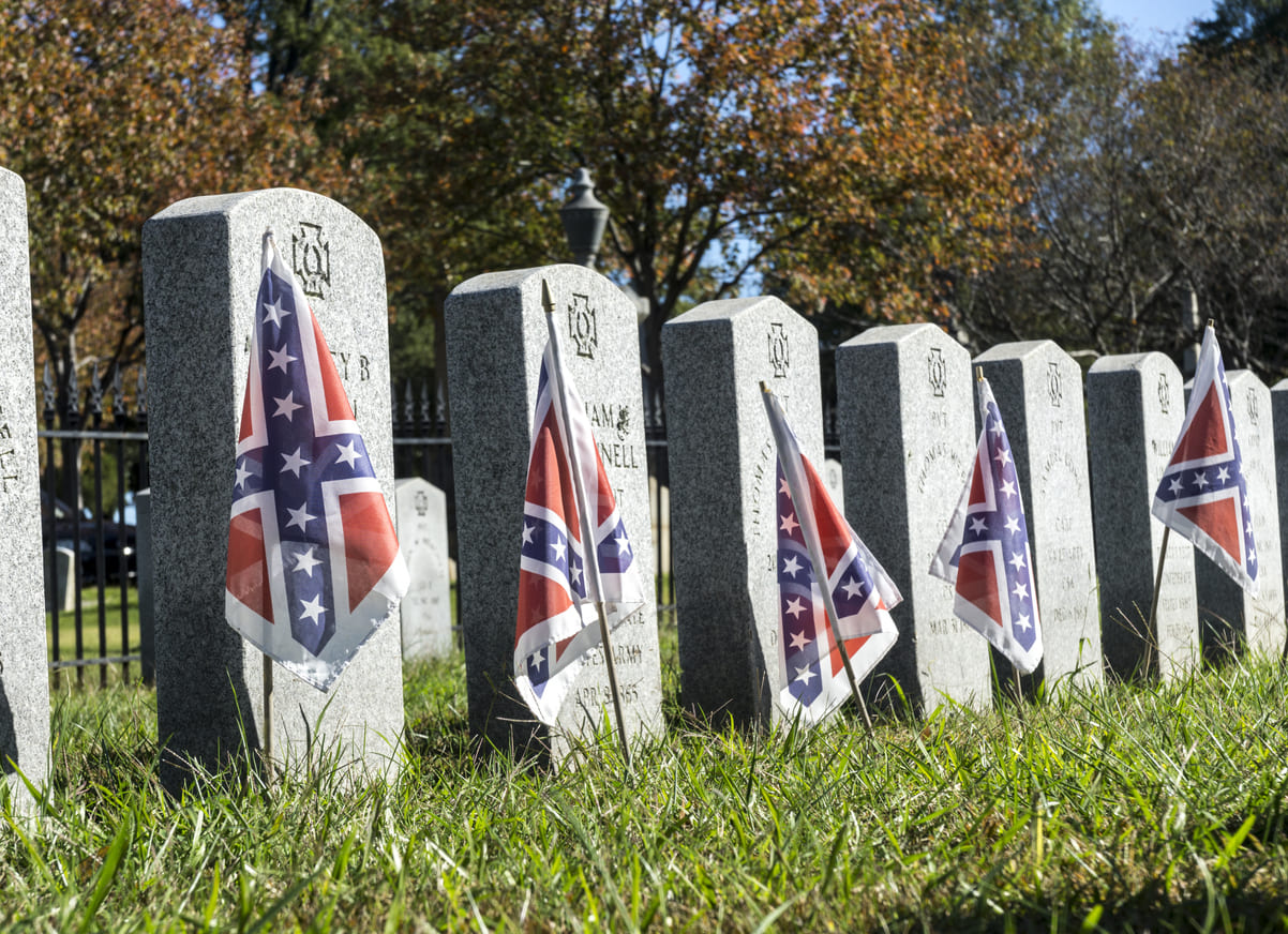 A cemetery displays numerous Confederate flags placed on gravestones, honoring Confederate soldiers.