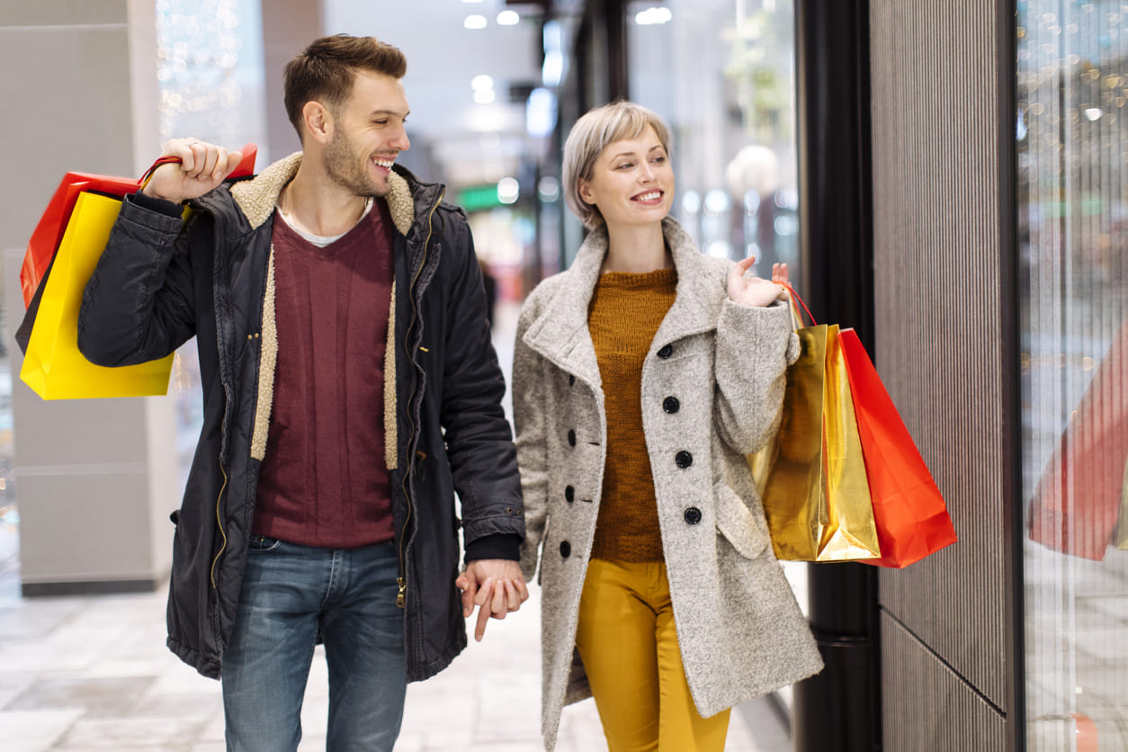 A happy couple strolls past a store, enjoying their Black Friday shopping.