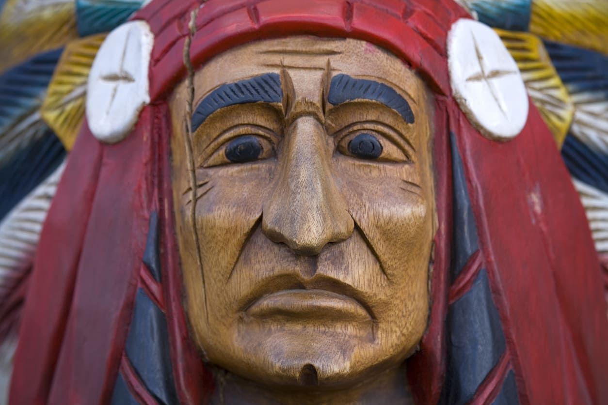 A detailed wooden carving depicts the face of a Native American figure, symbolizing cultural heritage and tradition.