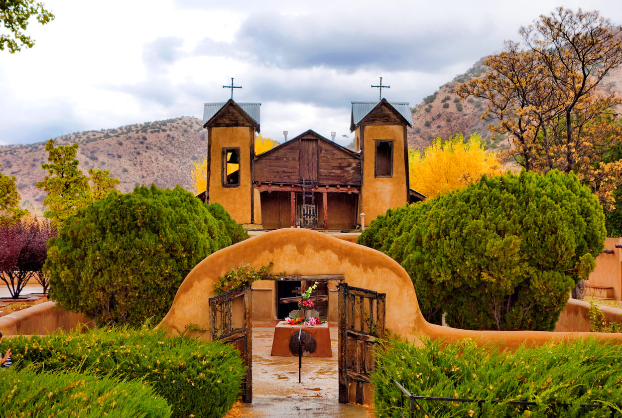 The historic Santuario de Chimayó church stands surrounded by lush greenery, inviting pilgrims seeking peace, healing, and reflection.