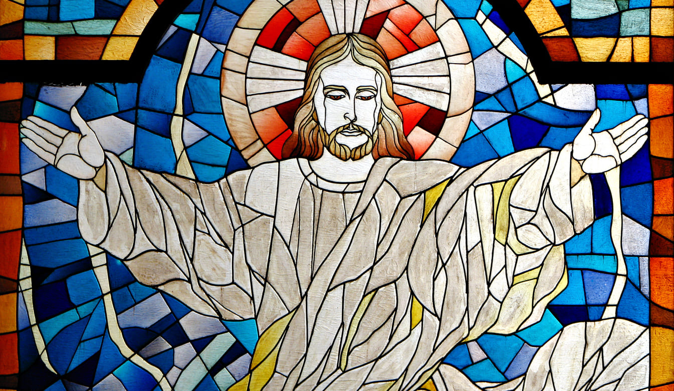 Stained-glass depiction of Jesus Christ with outstretched arms, symbolizing peace and divine resurrection.