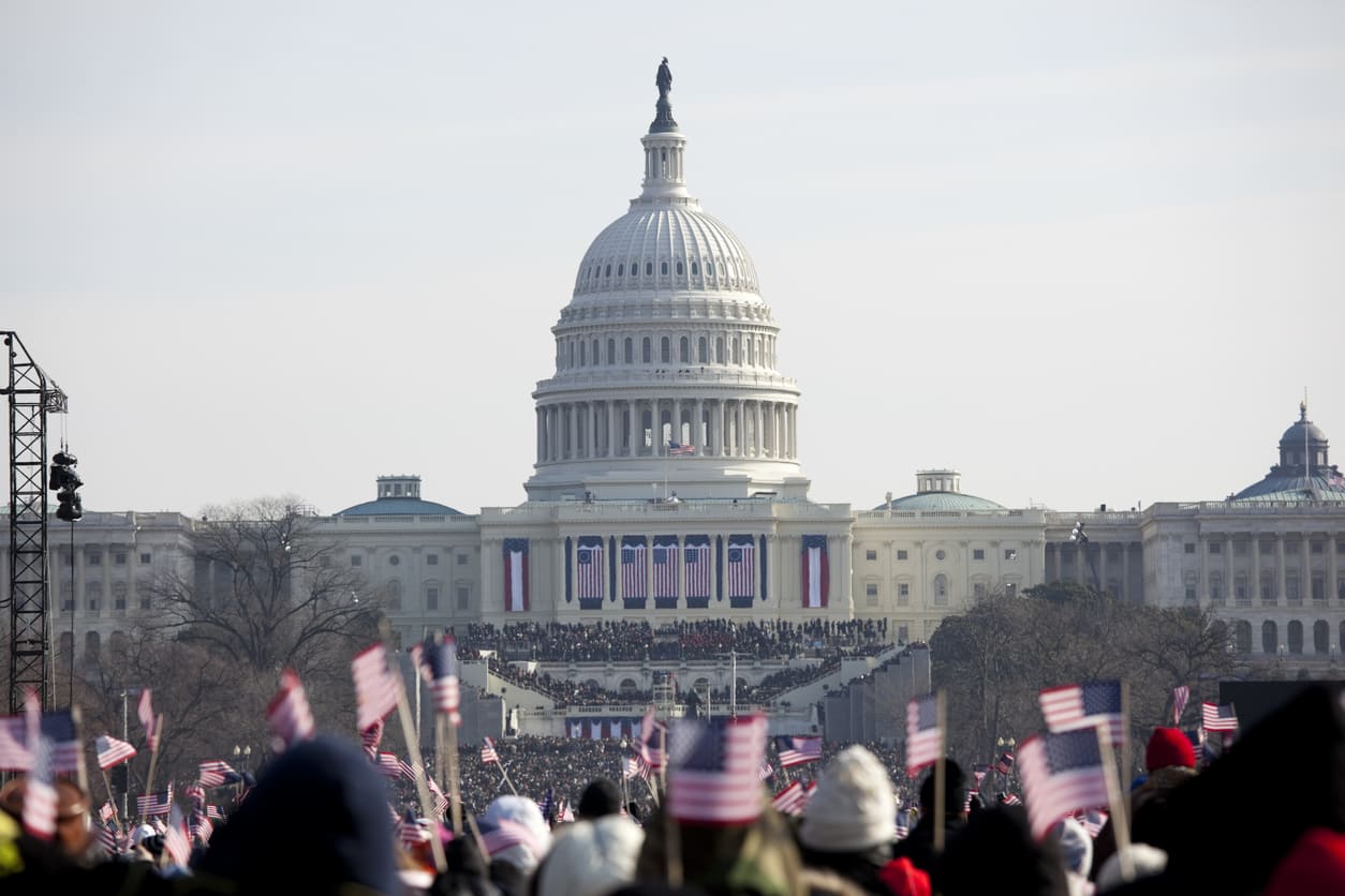 A large crowd waves American flags in front of the U.S. Capitol during the Inauguration Day ceremony.